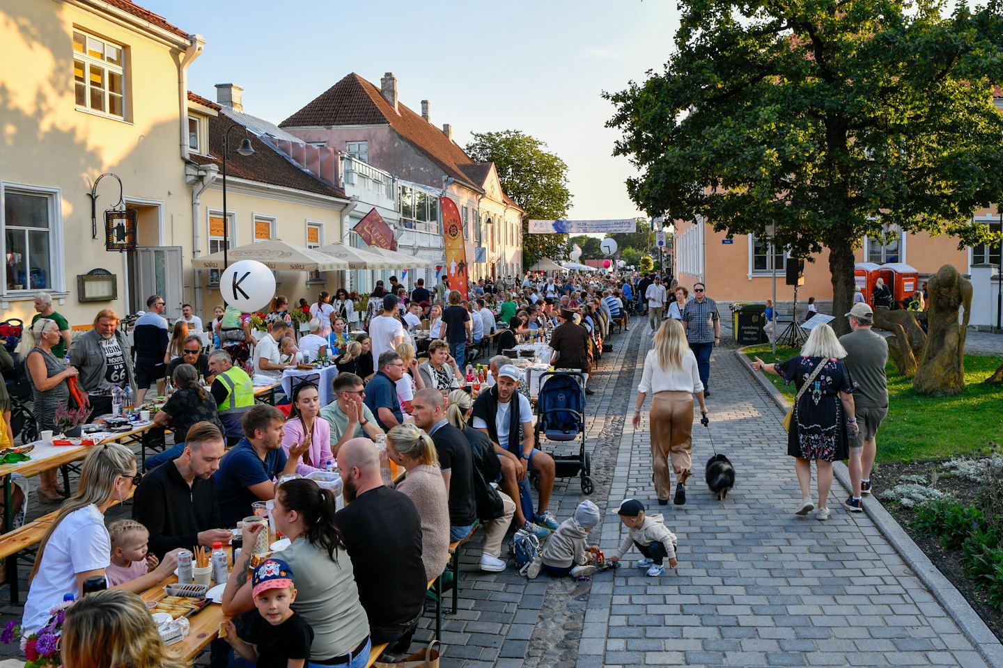 Folk minglar vid långa träbord under en utomhusgatufest.