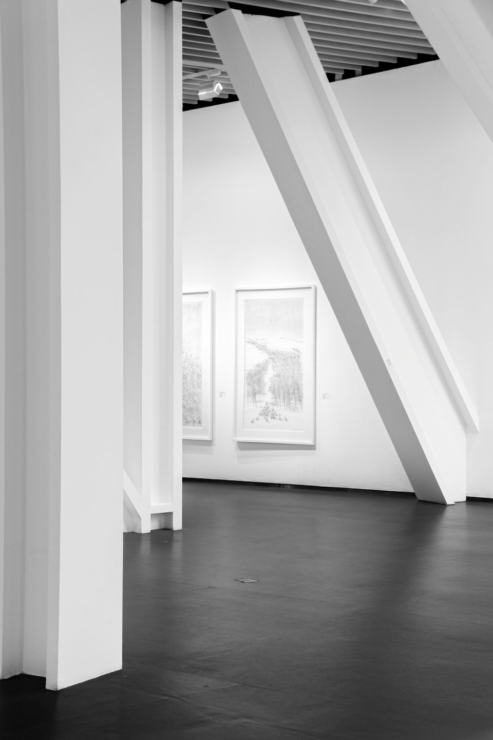 Två konstverk hänger på en vit vägg i ett minimalistiskt galleri.